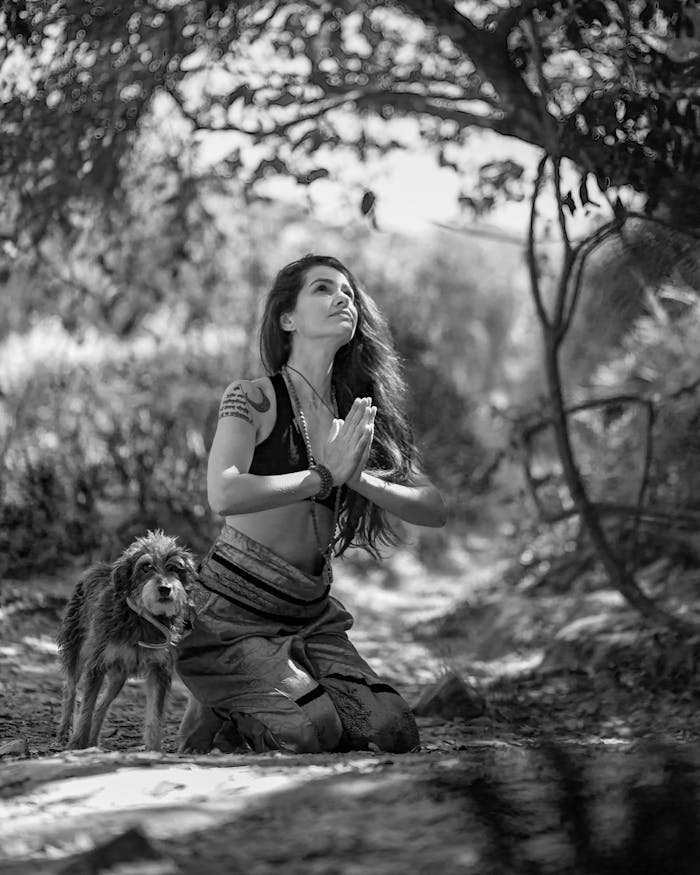 A woman meditates peacefully outdoors with her loyal dog by her side.